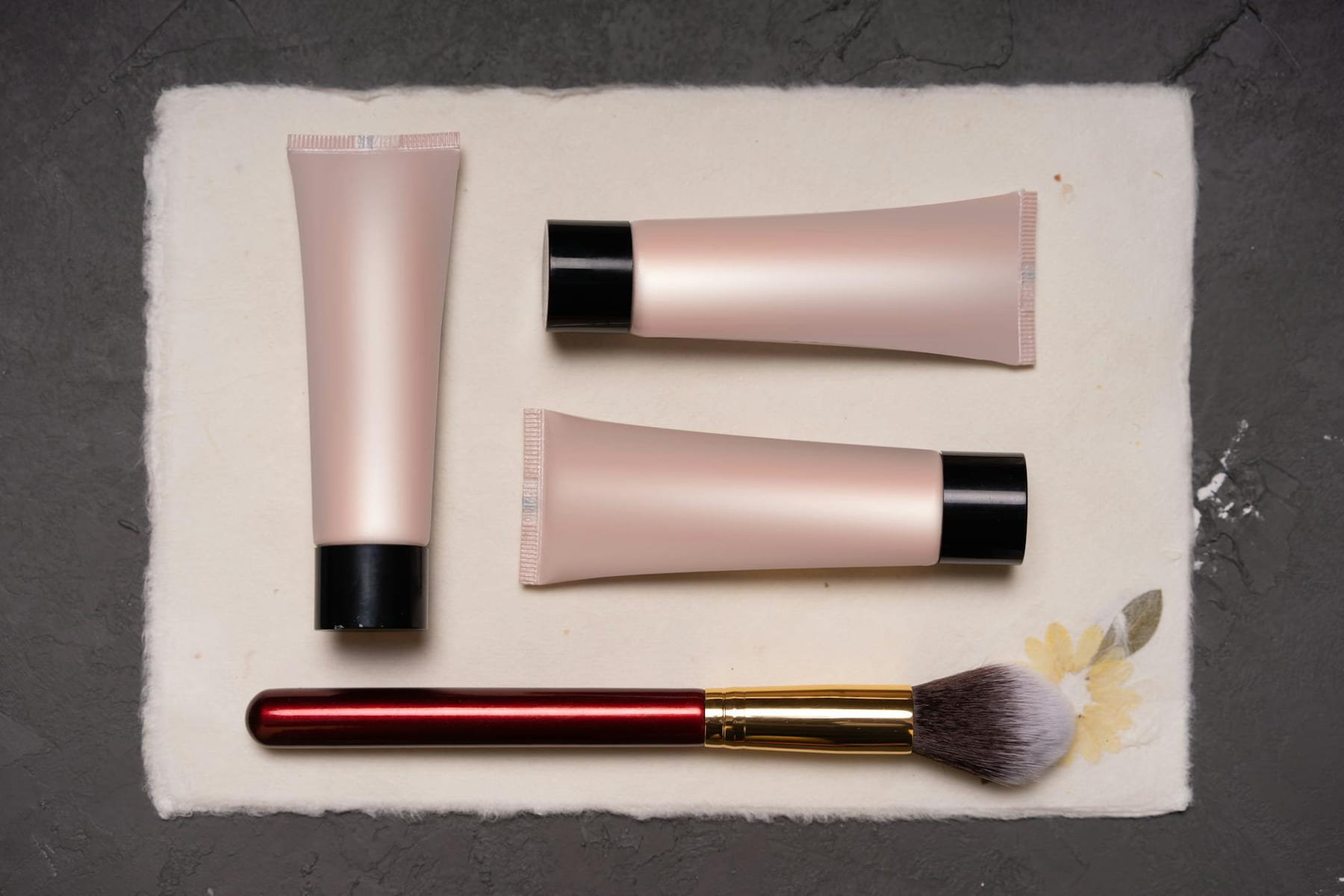 Beauty composition featuring cosmetic tubes and a makeup brush on a textured background. on Purely Polished