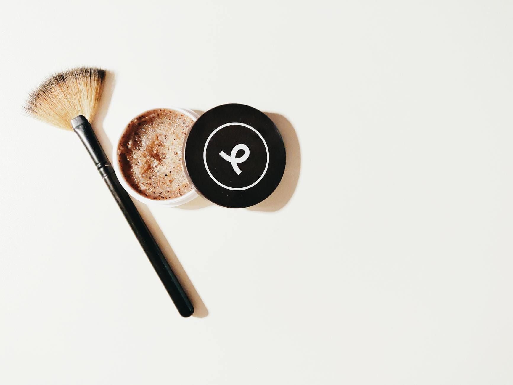Flat lay of a makeup brush and scrub container on a white surface, perfect for beauty and skincare themes. on Purely Polished