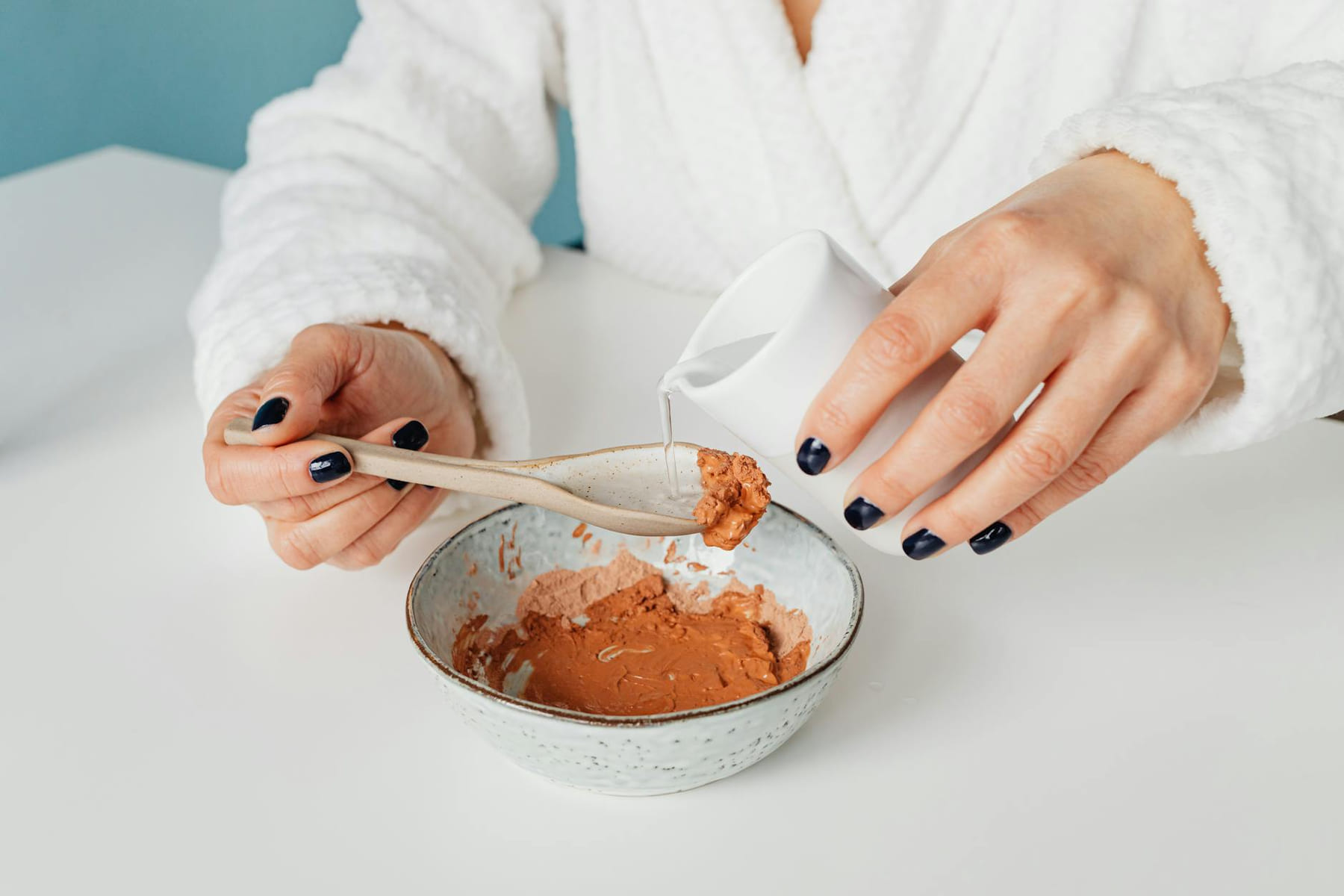 Close-up of a person mixing a natural clay mask with water for skincare. on Purely Polished