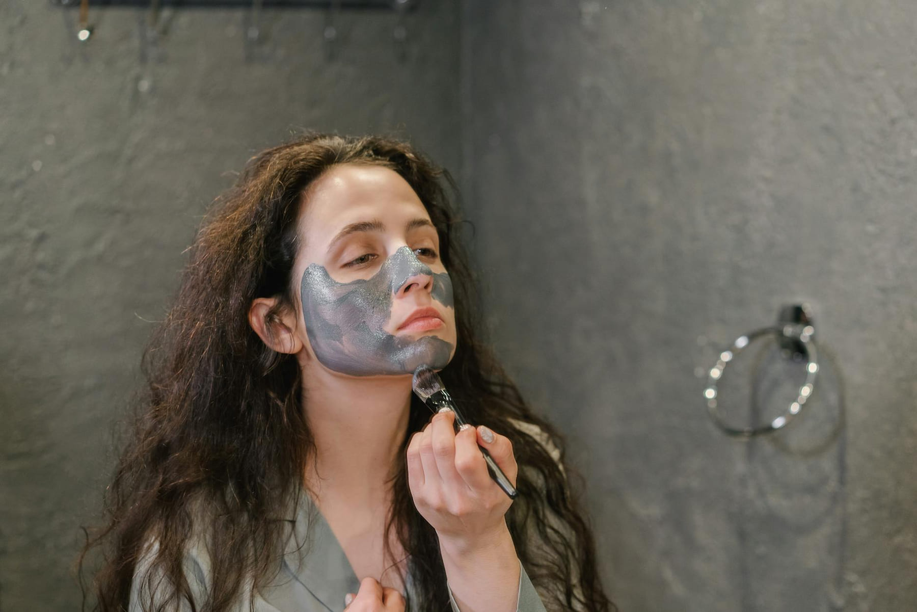 A woman applies a facial mask as part of her skincare routine in a modern bathroom. on Purely Polished
