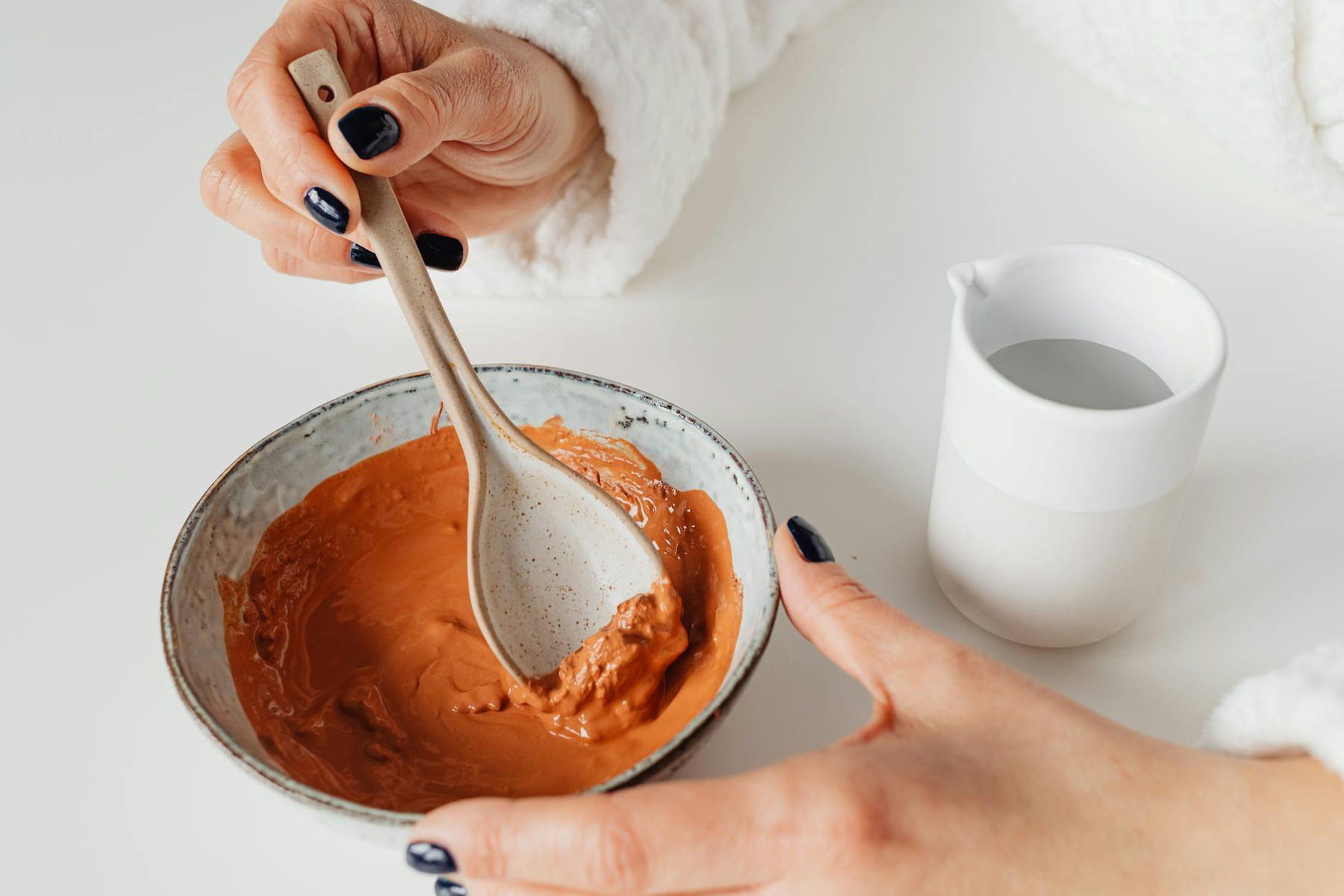 Close-up of hands mixing a natural skincare mask in a ceramic bowl, emphasizing beauty routine. on Purely Polished