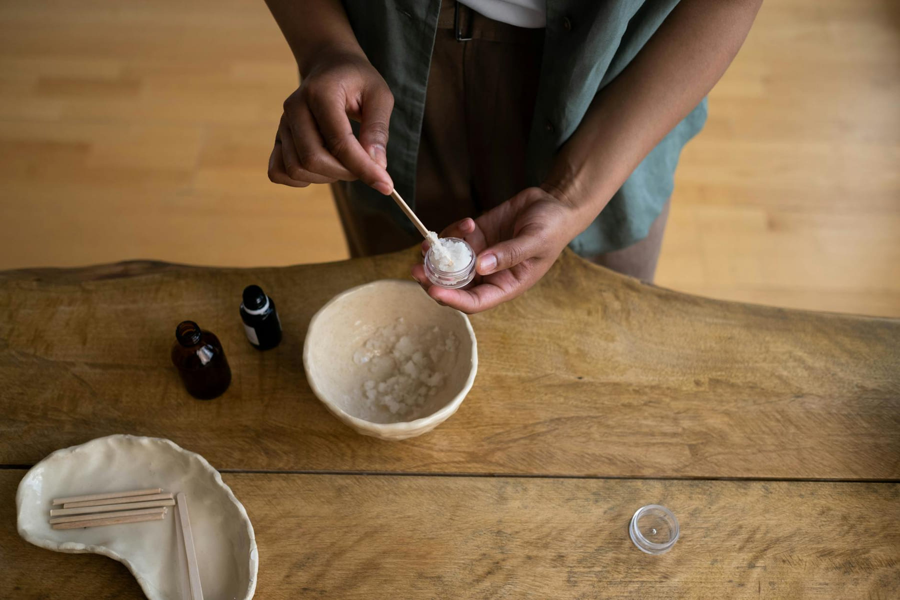 Hands transferring homemade skincare into a container on a wooden table. on Purely Polished