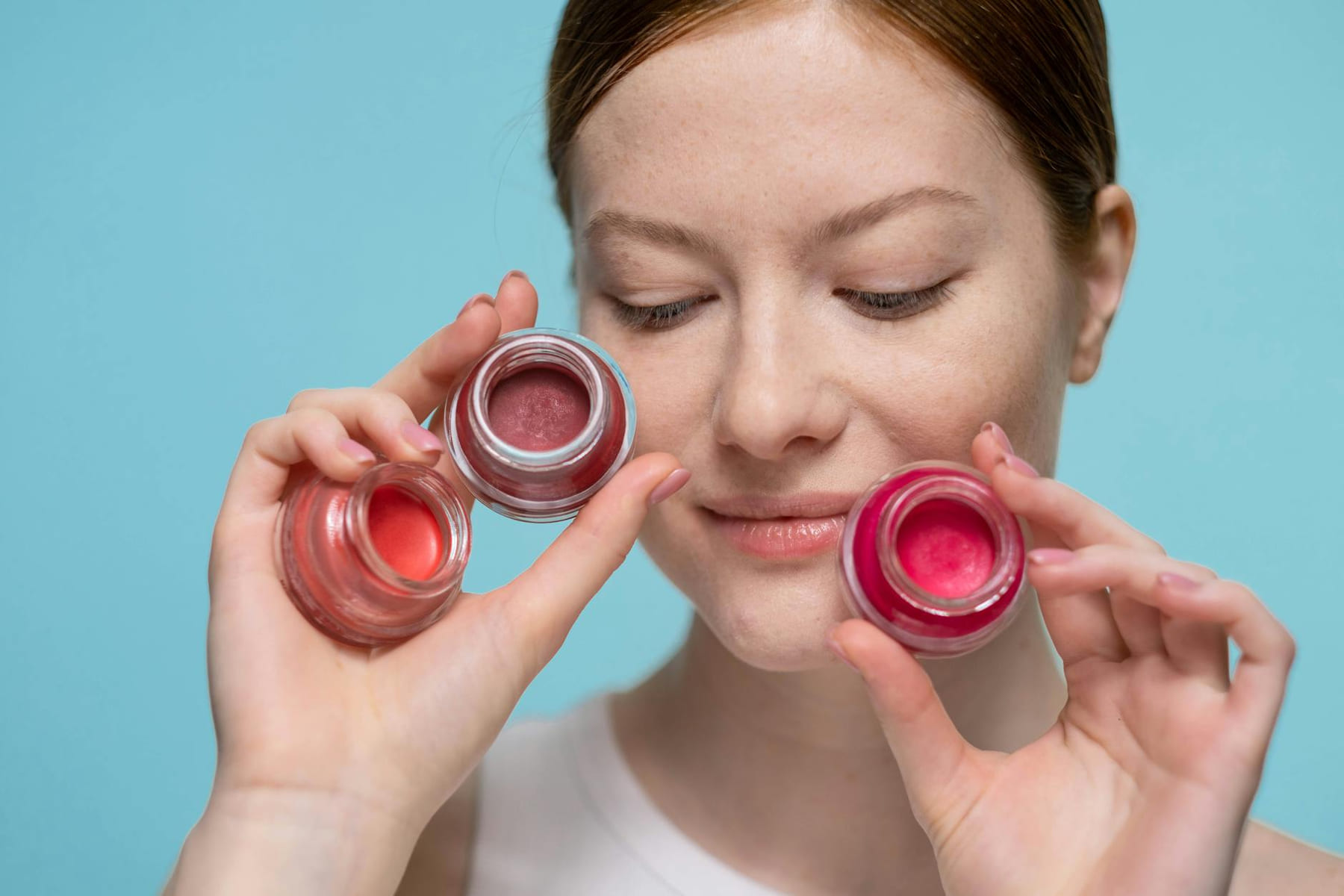 Close-up portrait of a woman holding colorful lip balm jars showcasing skincare and beauty products. on Purely Polished