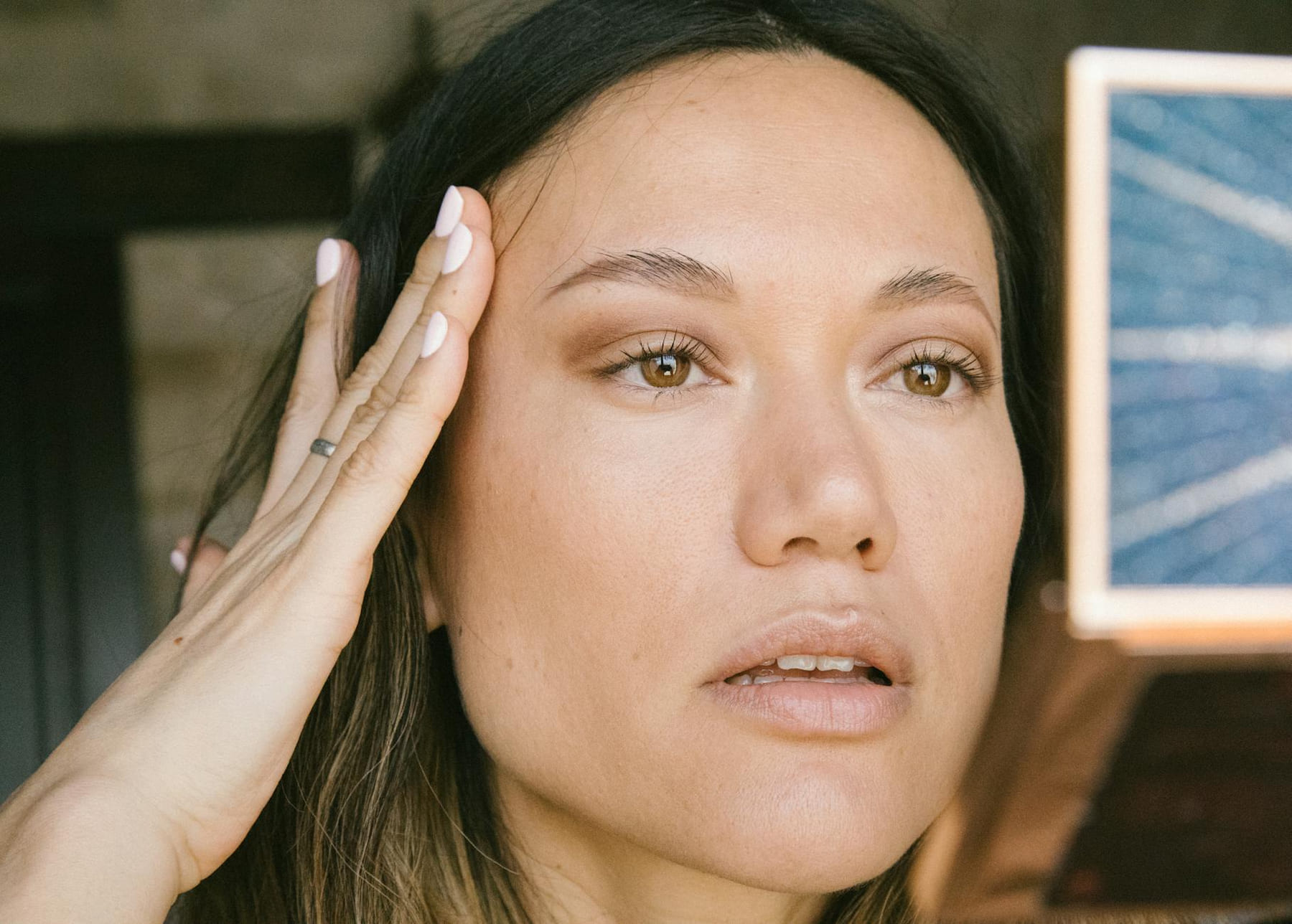 A natural close-up portrait of a woman applying makeup in an indoor setting. on Purely Polished
