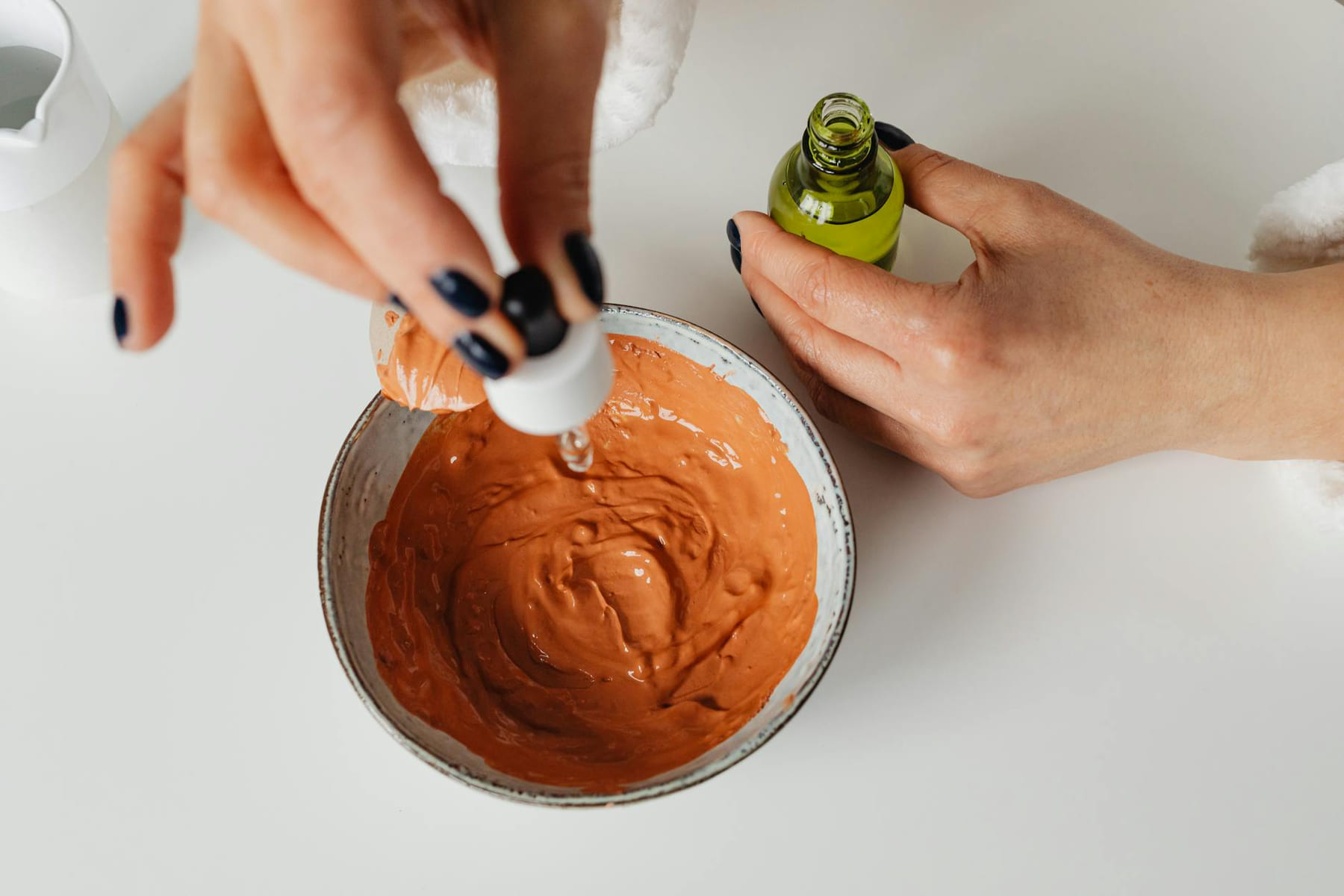 Close-up of hands blending clay mask with skincare essence in minimalist setting. on Purely Polished