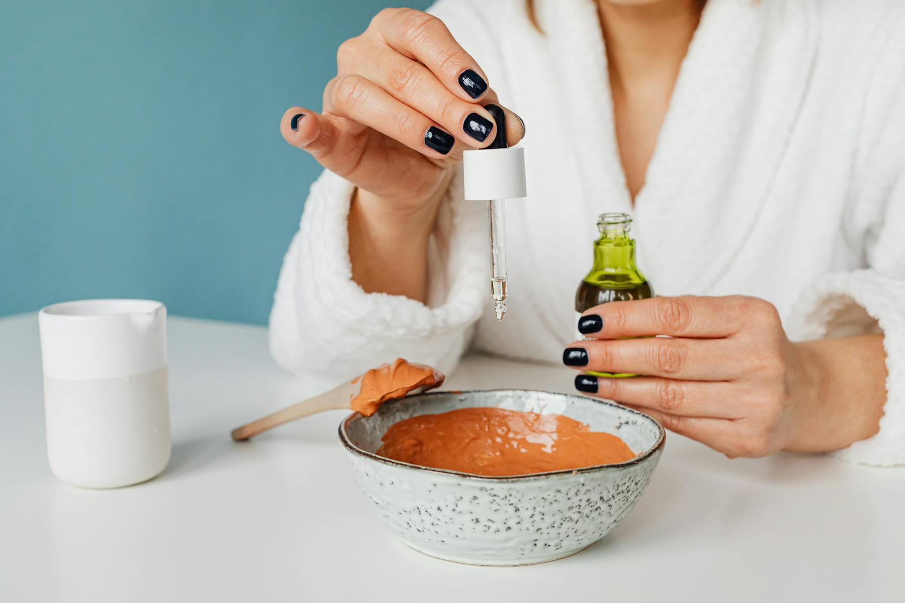 A woman in a bathrobe mixing ingredients for a DIY skincare mask using a pipette. on Purely Polished