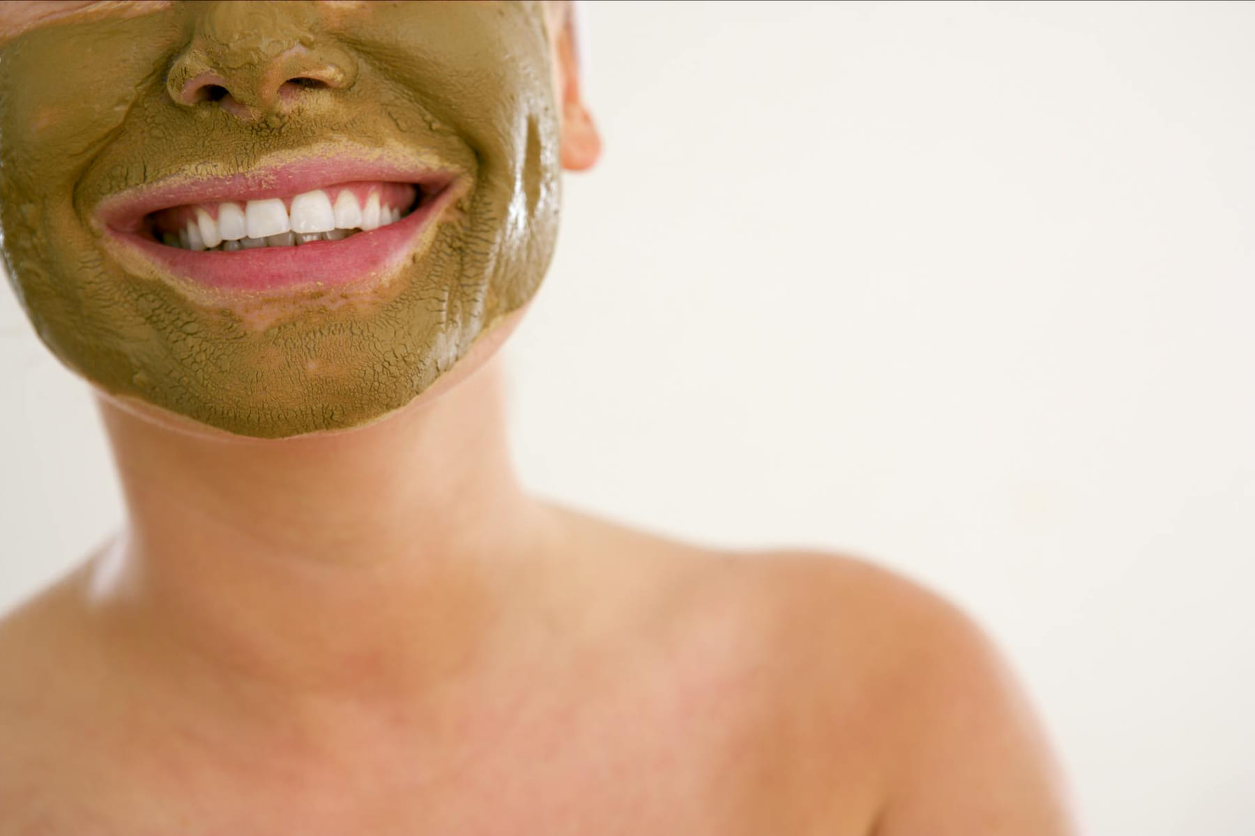 Close-up of a smiling woman applying a green cosmetic mask for skincare. on Purely Polished