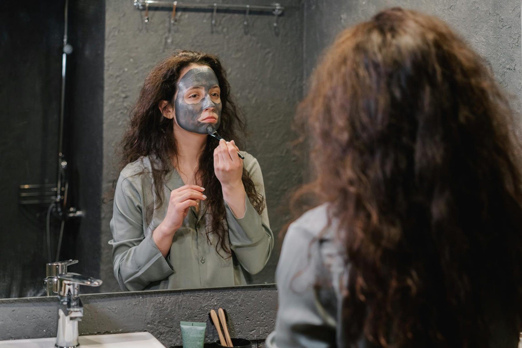 A woman applies a facial mask in the bathroom, focusing on skincare and wellness. on Purely Polished