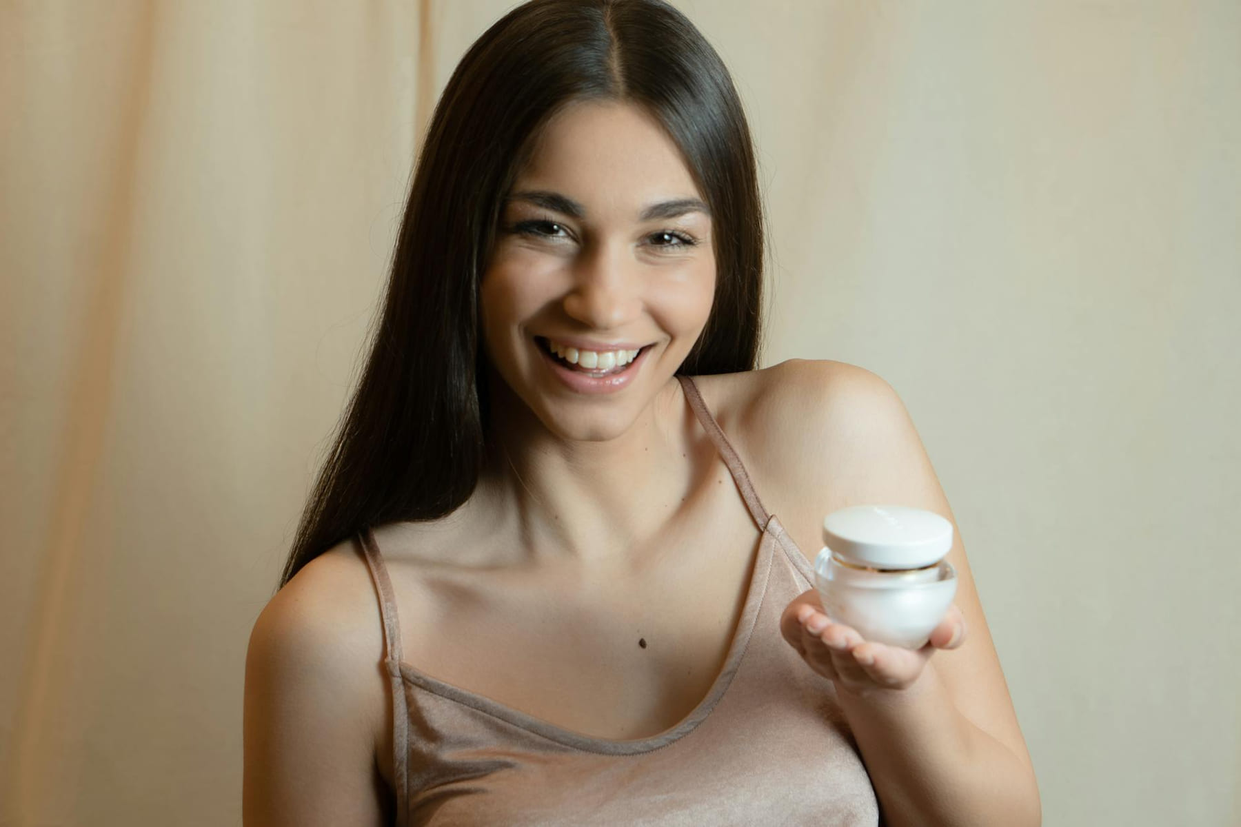 A smiling woman holding a skincare product, promoting beauty and wellness. on Purely Polished