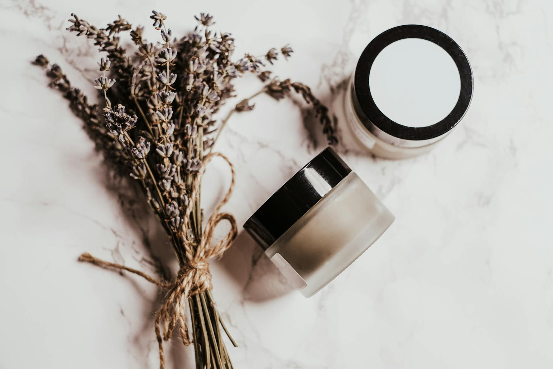 Elegant display of skincare products and lavender on a marble surface. on Purely Polished