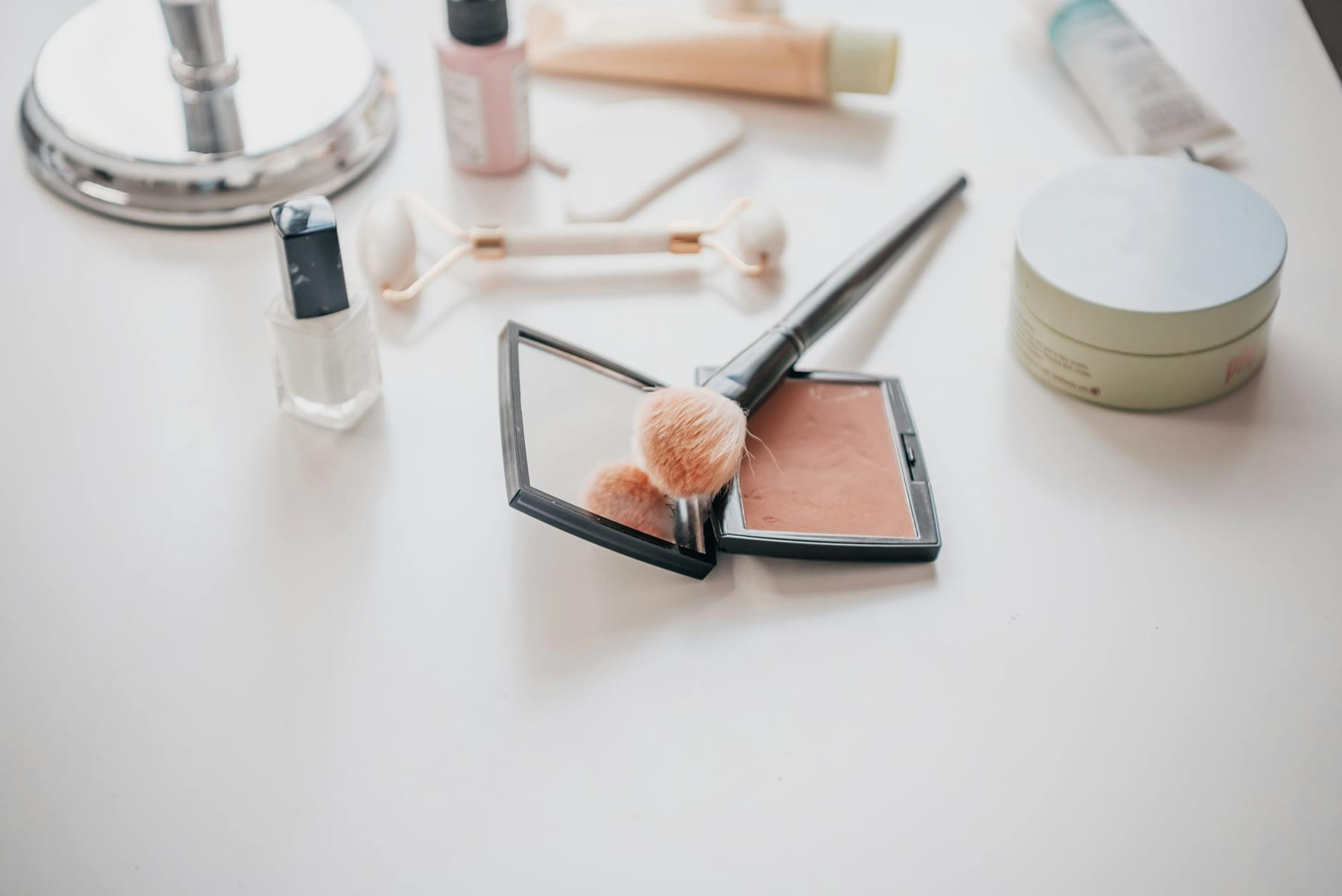 Image of makeup essentials including brushes, compacts, and creams on a vanity table. on Purely Polished