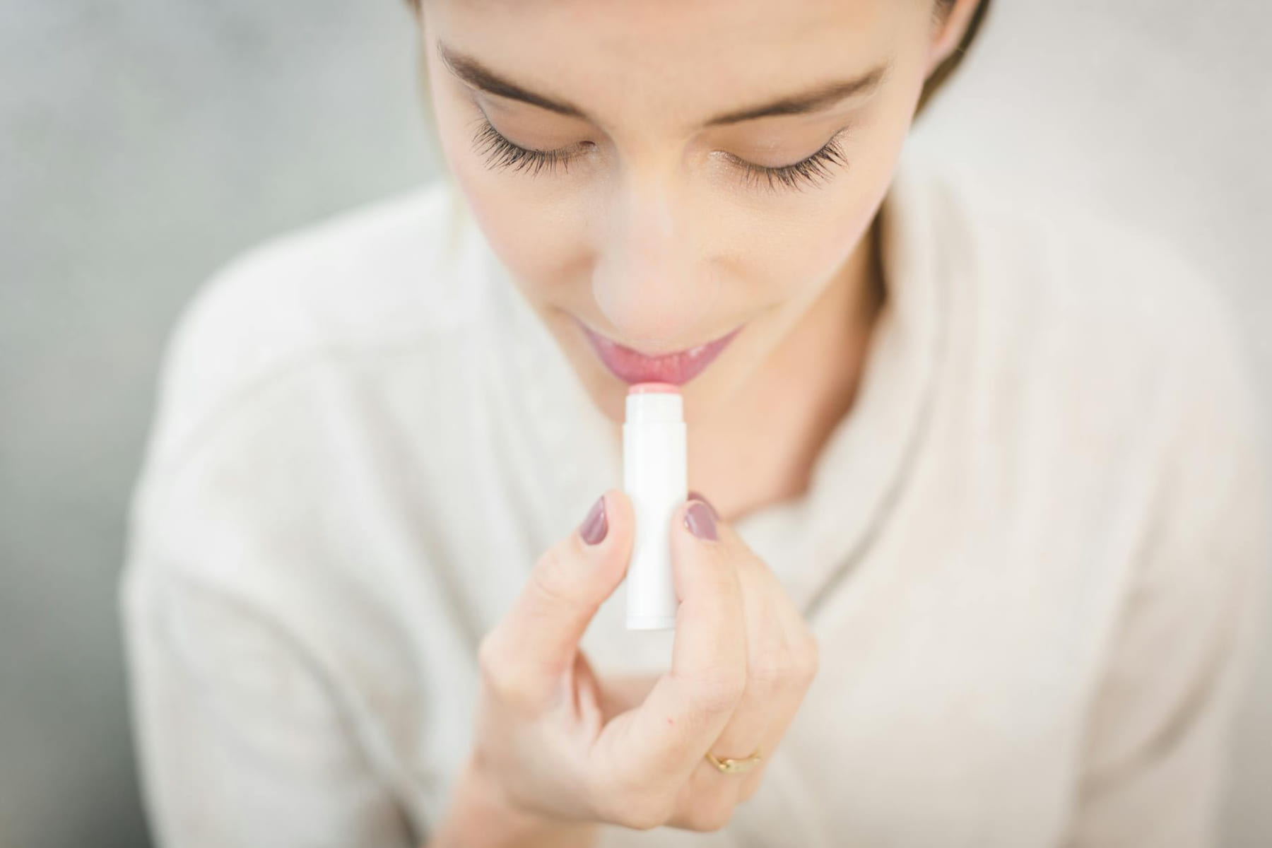 A close-up of a woman applying light-colored lip balm for moisturizing. on Purely Polished